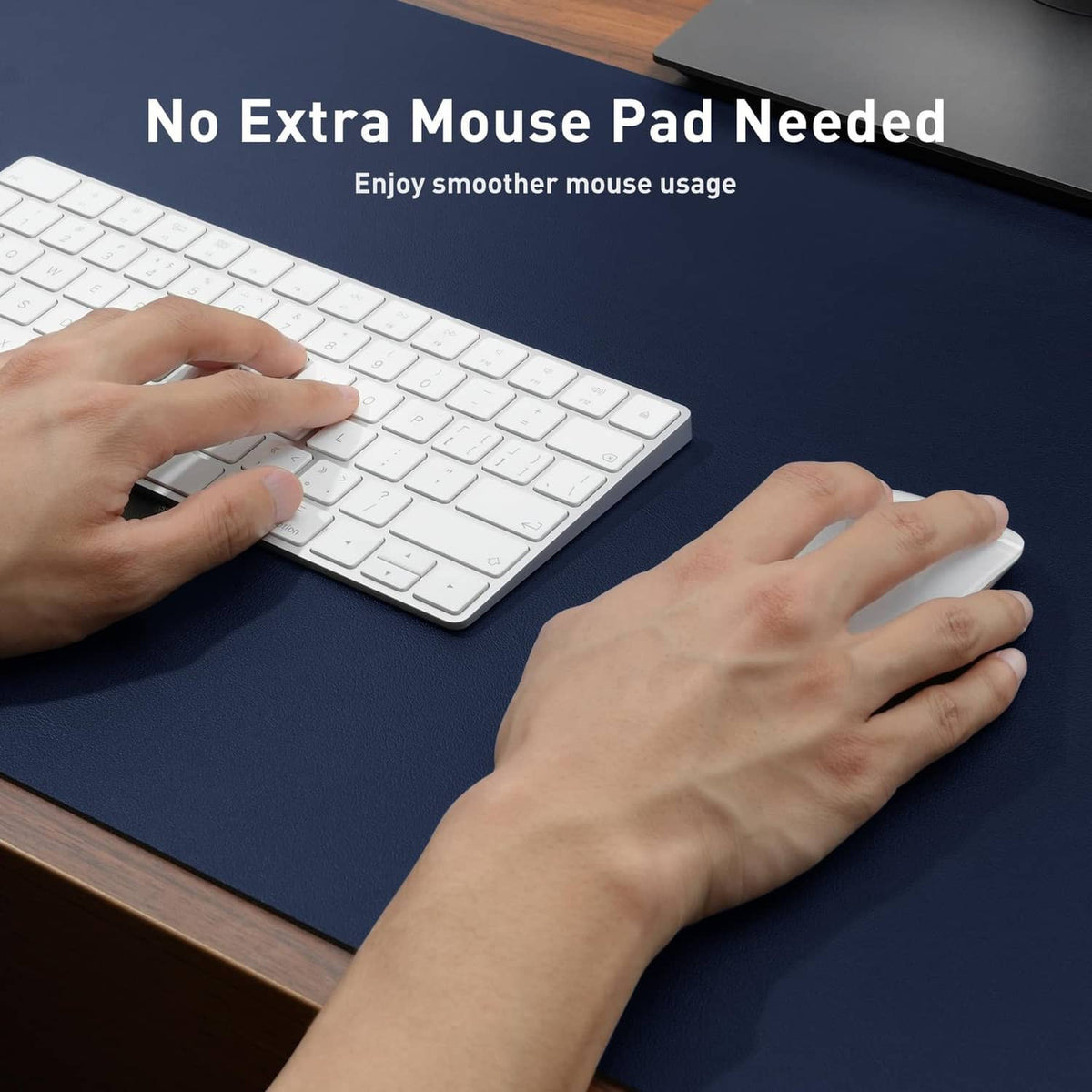 Dark blue desk pad protector with hands using a keyboard and mouse on the surface.
