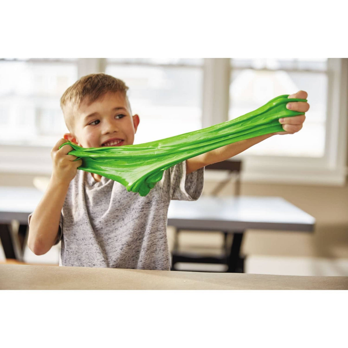 Child stretching bright green slime while holding a school glue bottle