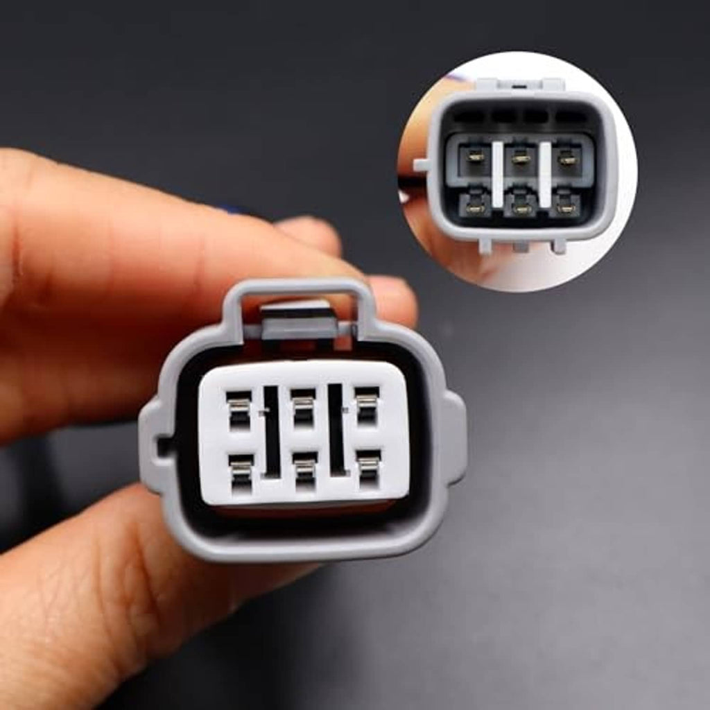 Hand holding a gray 6-pin headlight connector plug with visible terminal pins