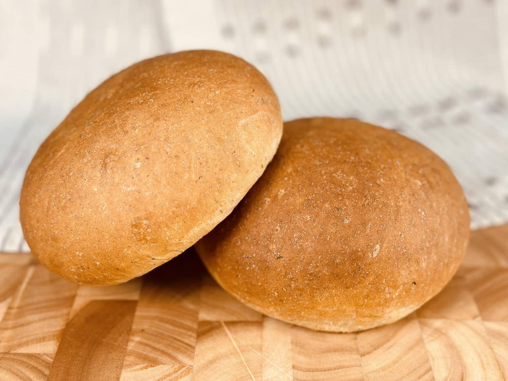 Two golden potato bread rolls on a wood board