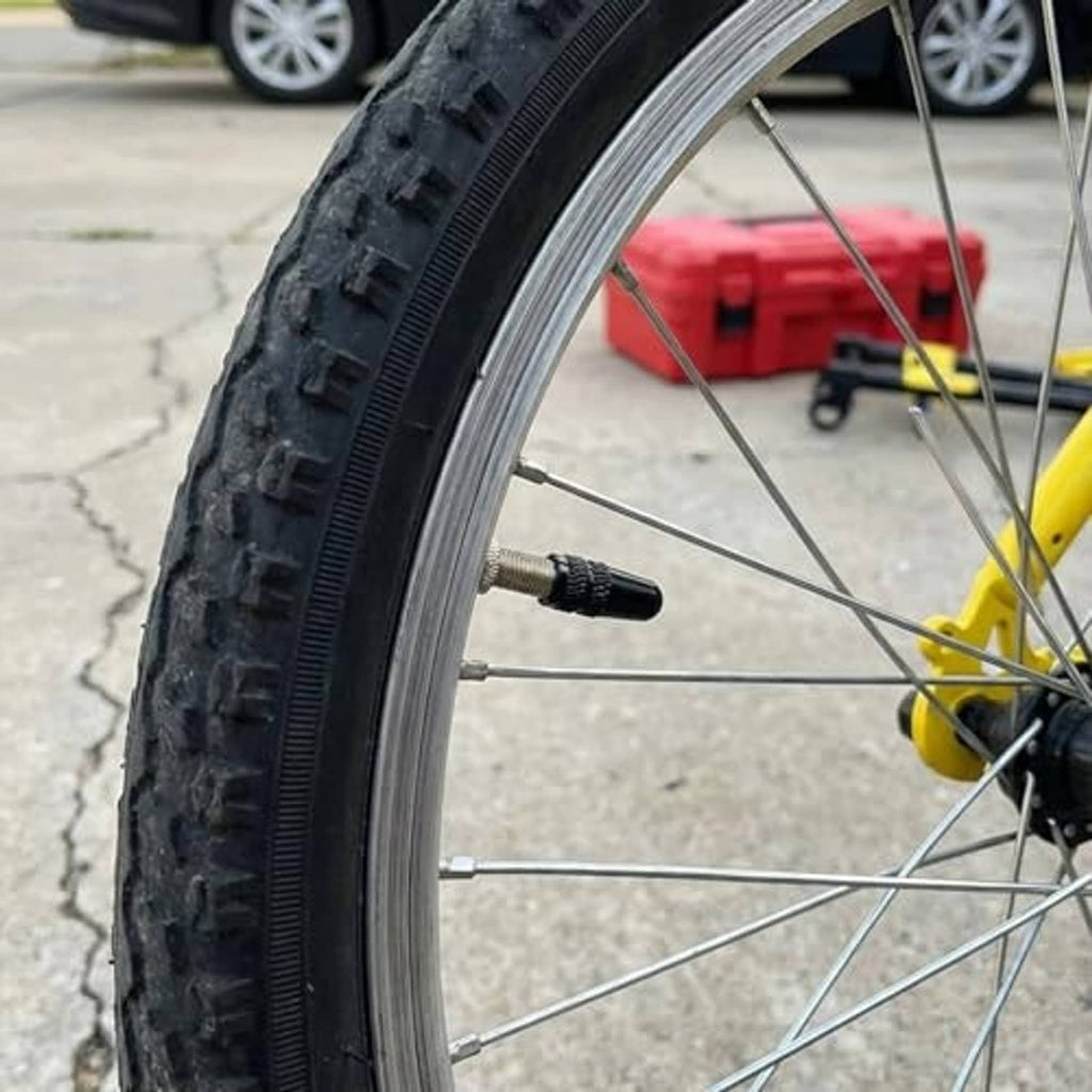 Black knurled Presta valve cap installed on a bicycle front wheel rim