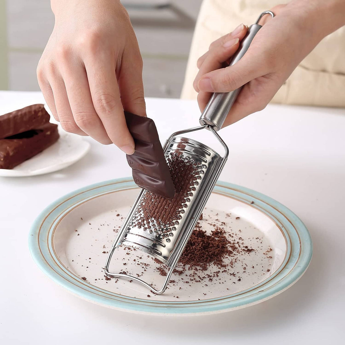 Stainless steel box grater held over a plate, grating fine chocolate