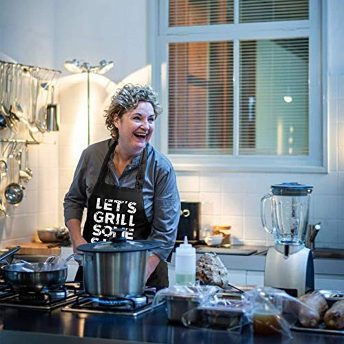 Black BBQ apron with "LET'S GRILL SOME SHIT" worn in kitchen while cooking