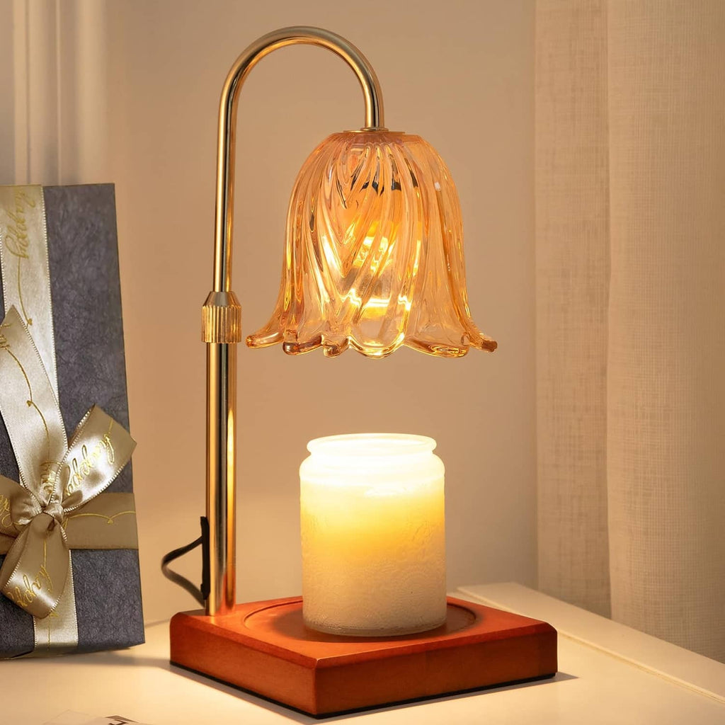Gold flameless candle lamp with glass flower shade and lit jar candle on wooden base