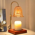 Gold flameless candle lamp with glass flower shade and lit jar candle on wooden base