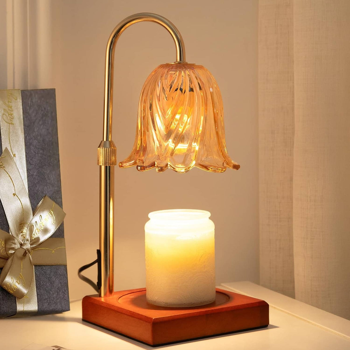 Gold flameless candle lamp with glass flower shade and lit jar candle on wooden base
