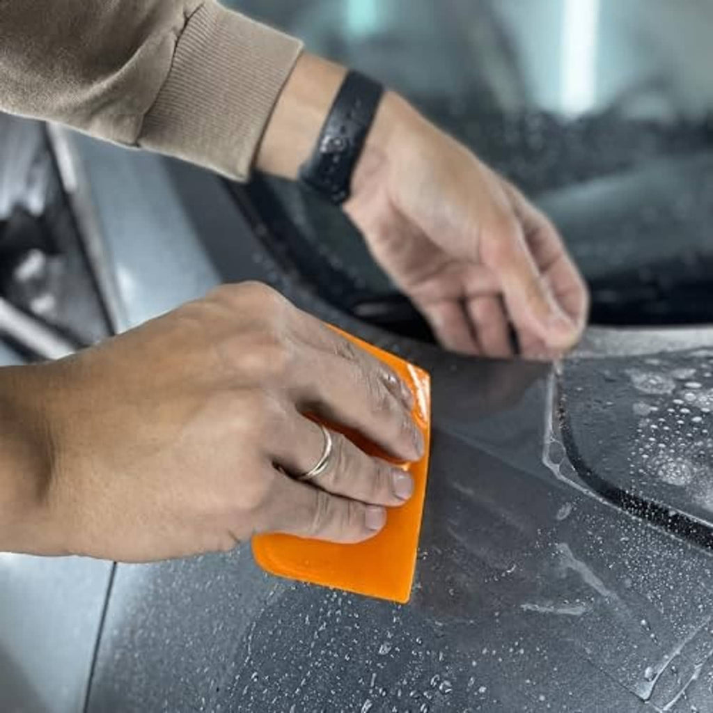 Hands using an orange TPU squeegee on a glass surface