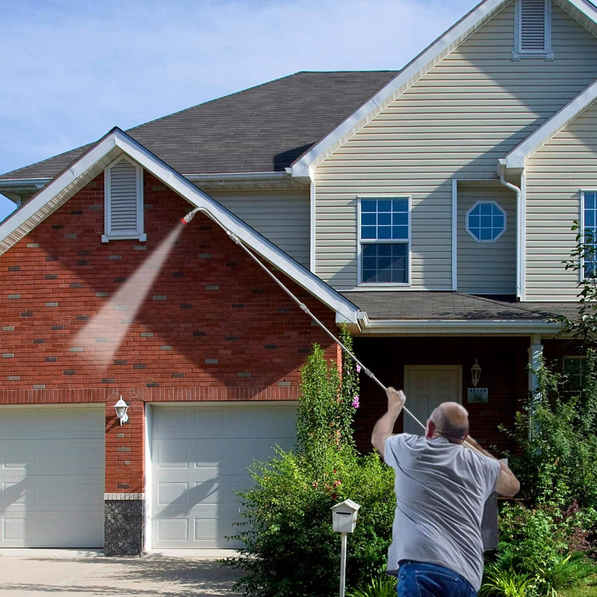 Pressure washer extension wand spraying water at a house exterior wall