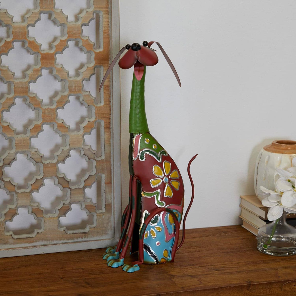 Decorative metal dog garden statue with red face and colorful floral panels, displayed indoors
