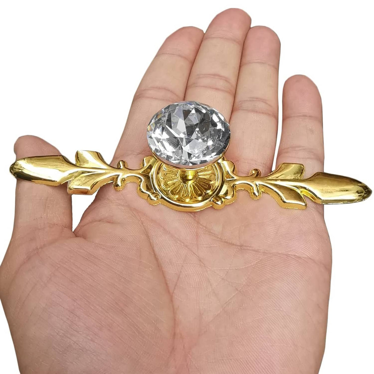 Gold decorative crystal glass knob with clear faceted round stone and leaf arms, held in hand