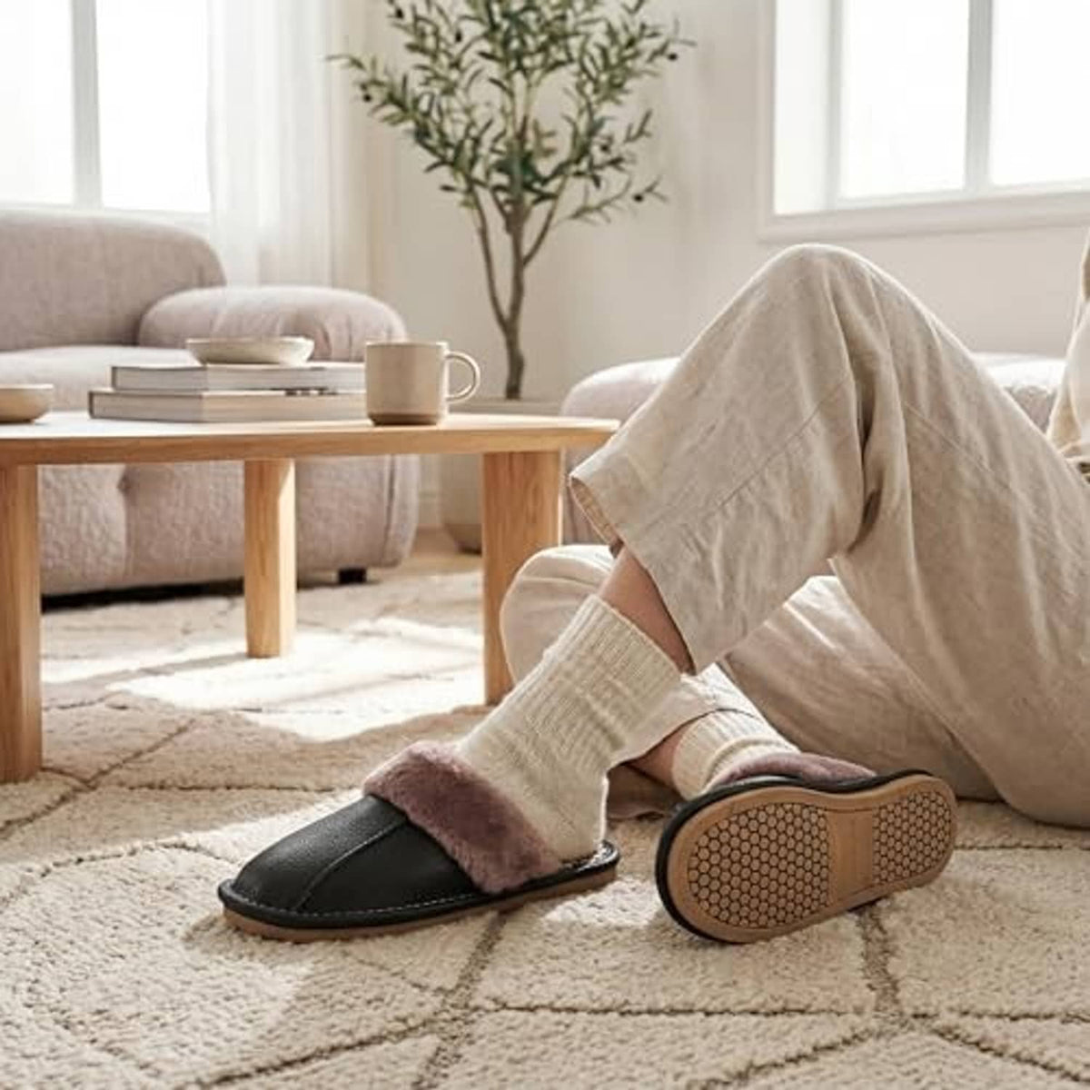 Unisex black leather slippers with plush taupe lining and textured outsole on carpet.
