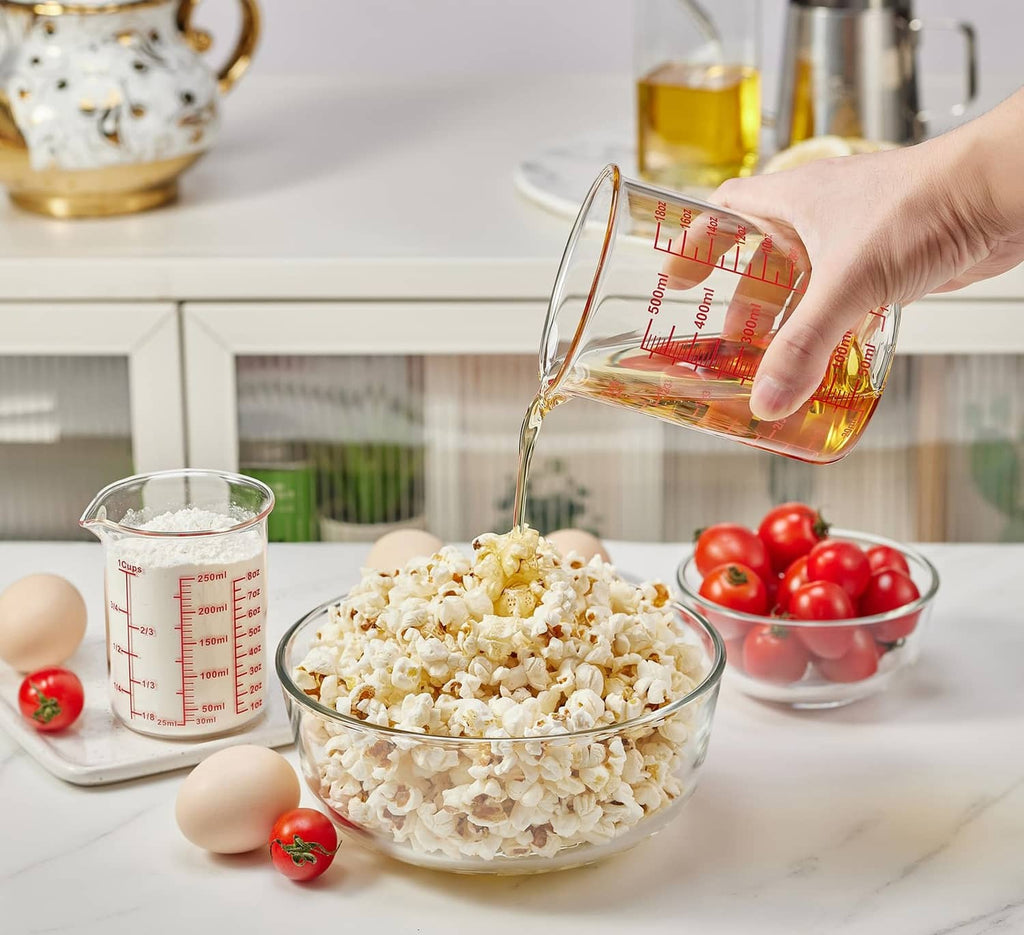 Clear glass measuring cup with red measurement lines and V-shaped spout, held and pouring