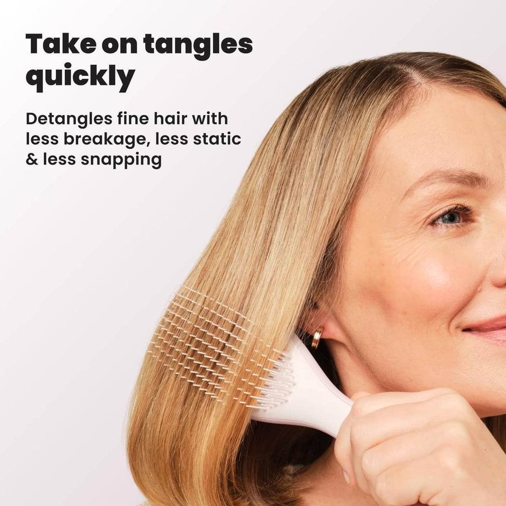 Woman using pink detangling hairbrush on blonde hair, close-up