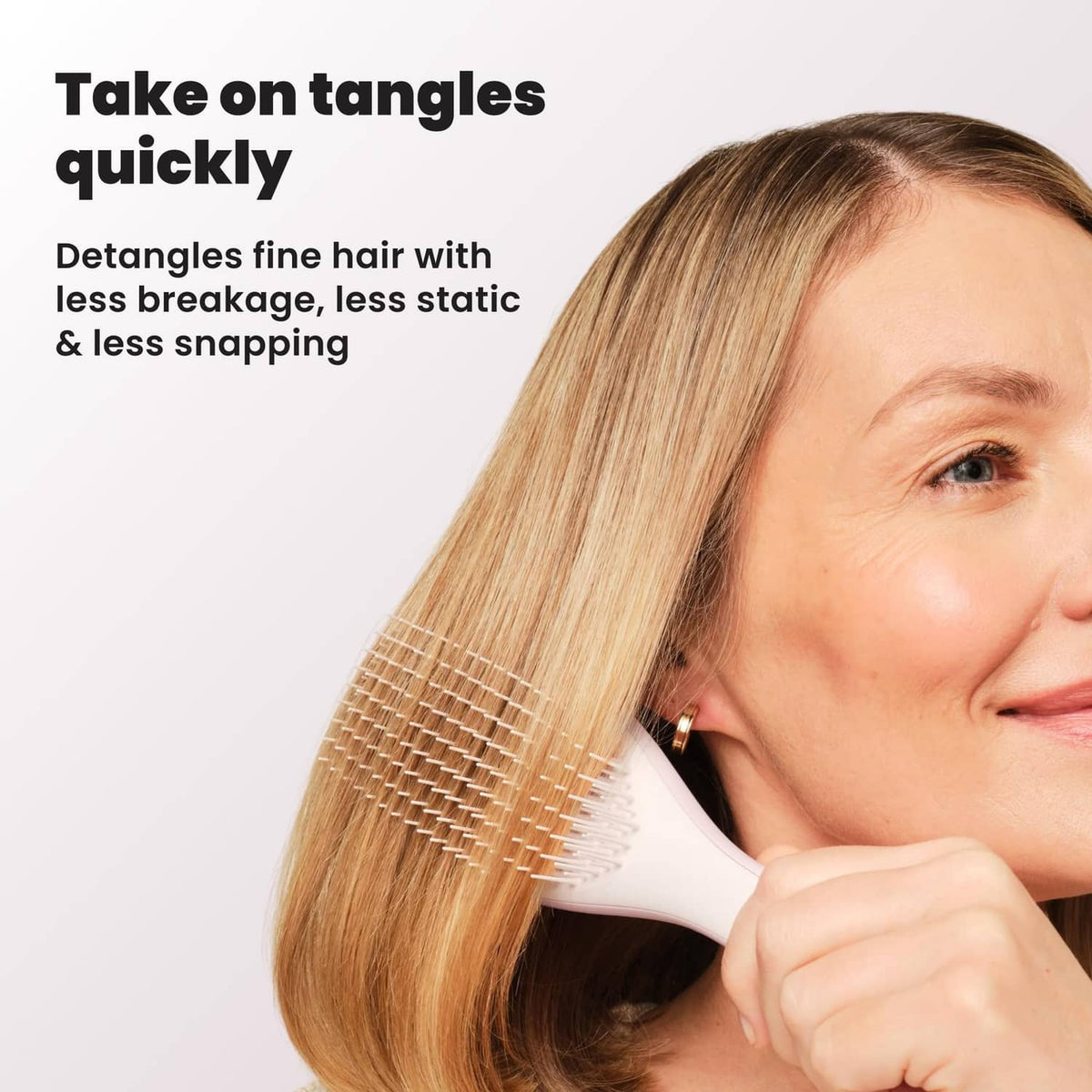 Woman using pink detangling hairbrush on blonde hair, close-up