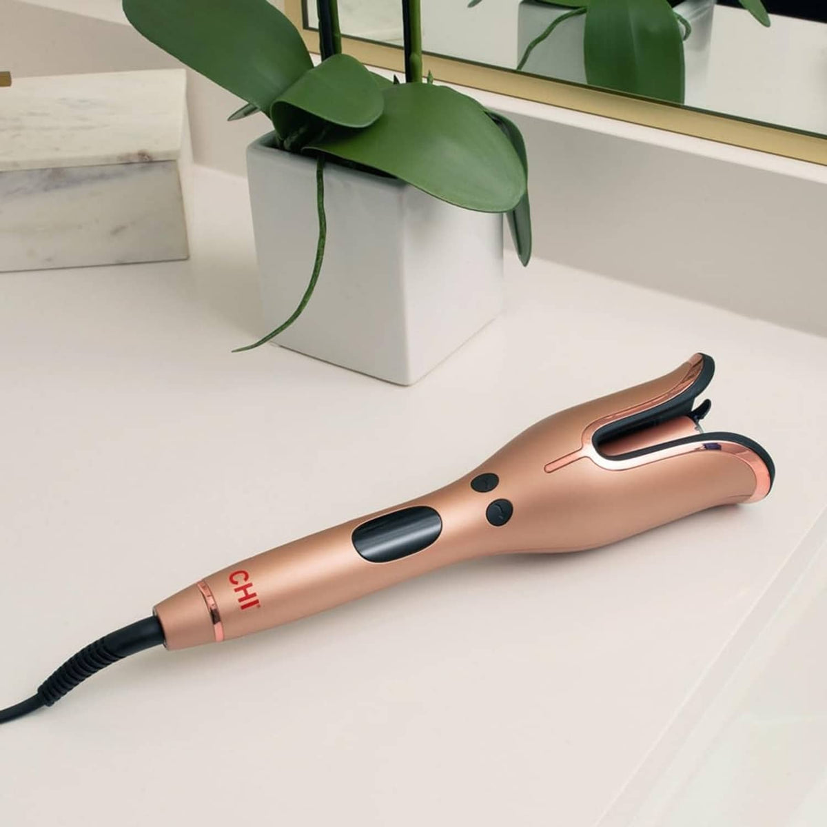 Rose gold rotating curling iron with black cable, two button controls, and U-shaped barrel