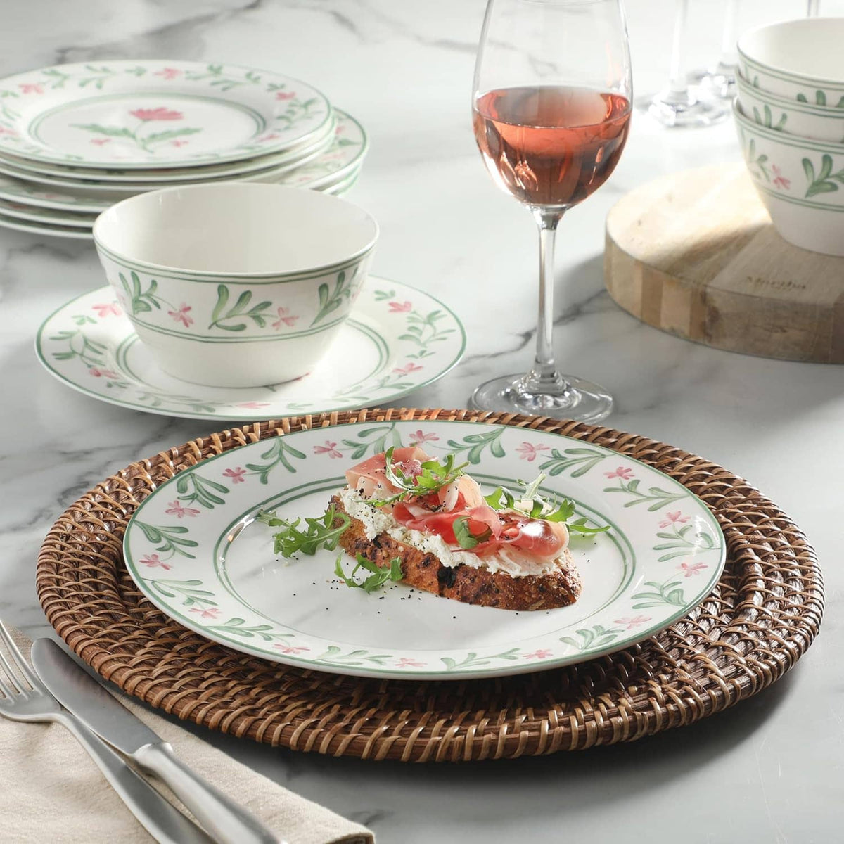 Floral dinner plate with cured meat and greens, plus stacked bowls in green-pink pattern
