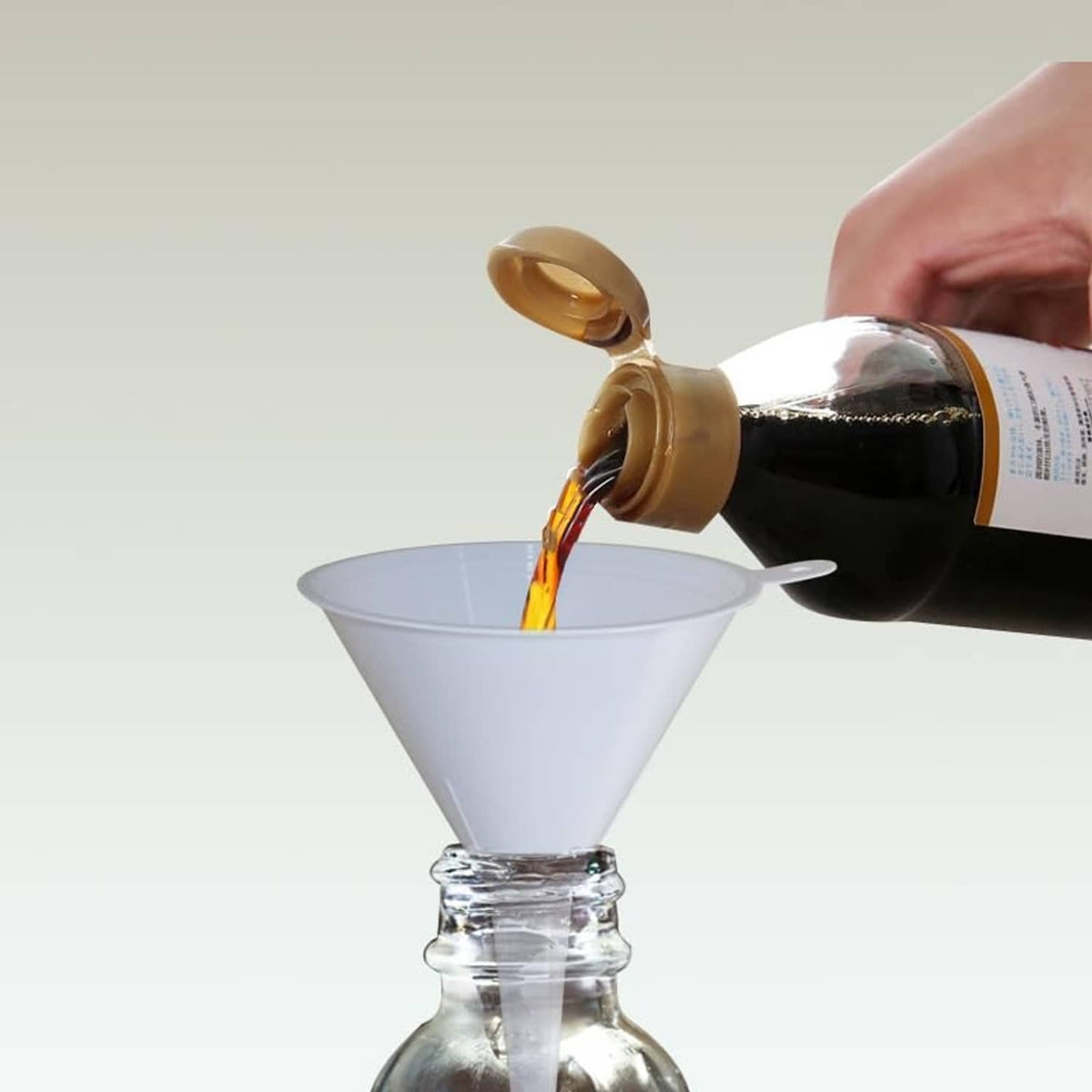White plastic funnel with side spout pouring oil from a bottle
