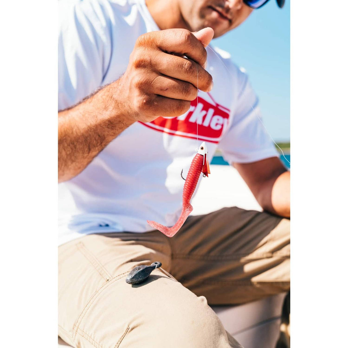 Red soft plastic worm lure with hook held between fingers
