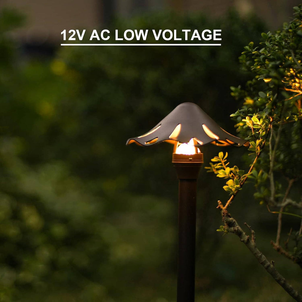 Single lit low-voltage LED pathway light with spike base beside outdoor shrubs