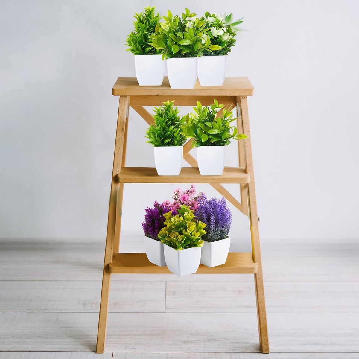 Artificial mini plants in white pots on a wooden display stand, green and purple blooms