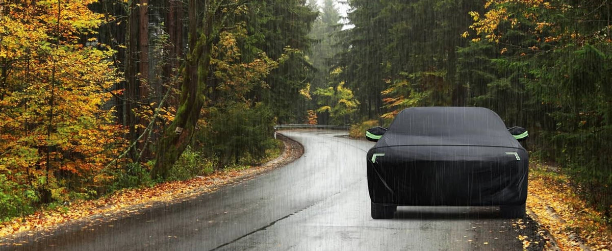 Black car cover fitted over a sedan parked on a road in autumn scenery