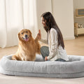 Grey oval human dog bed with soft plush rim, shown with dog and person relaxing.
