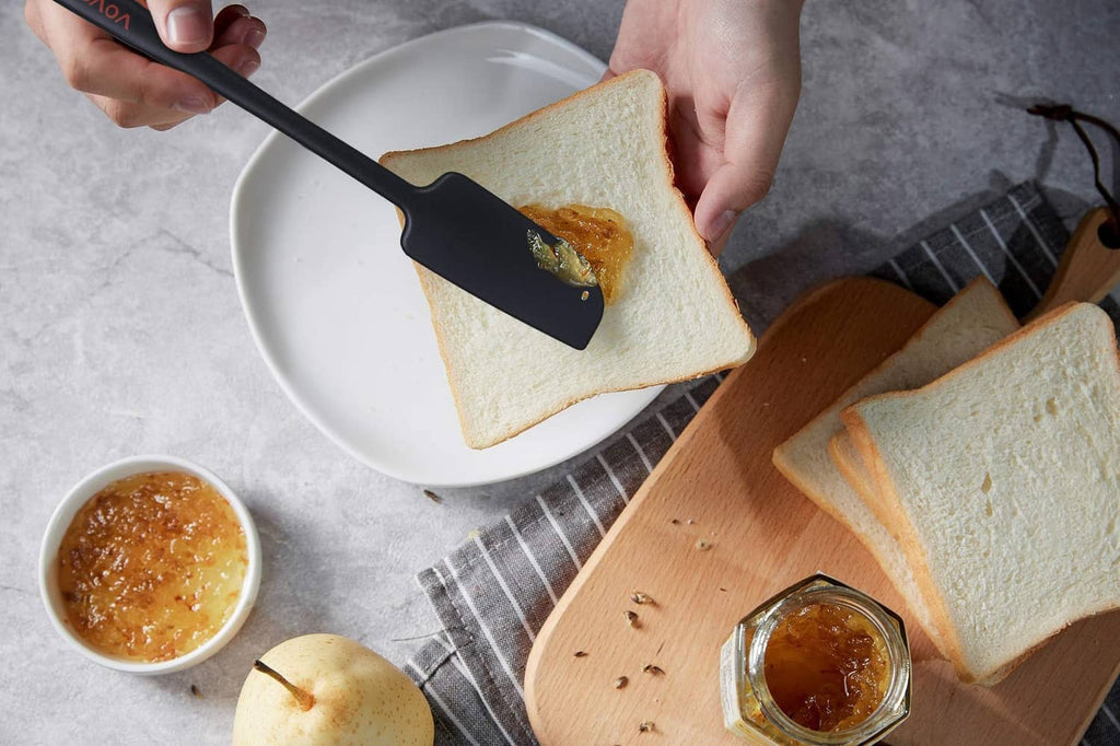 Black silicone spatula spreading topping on toast slices