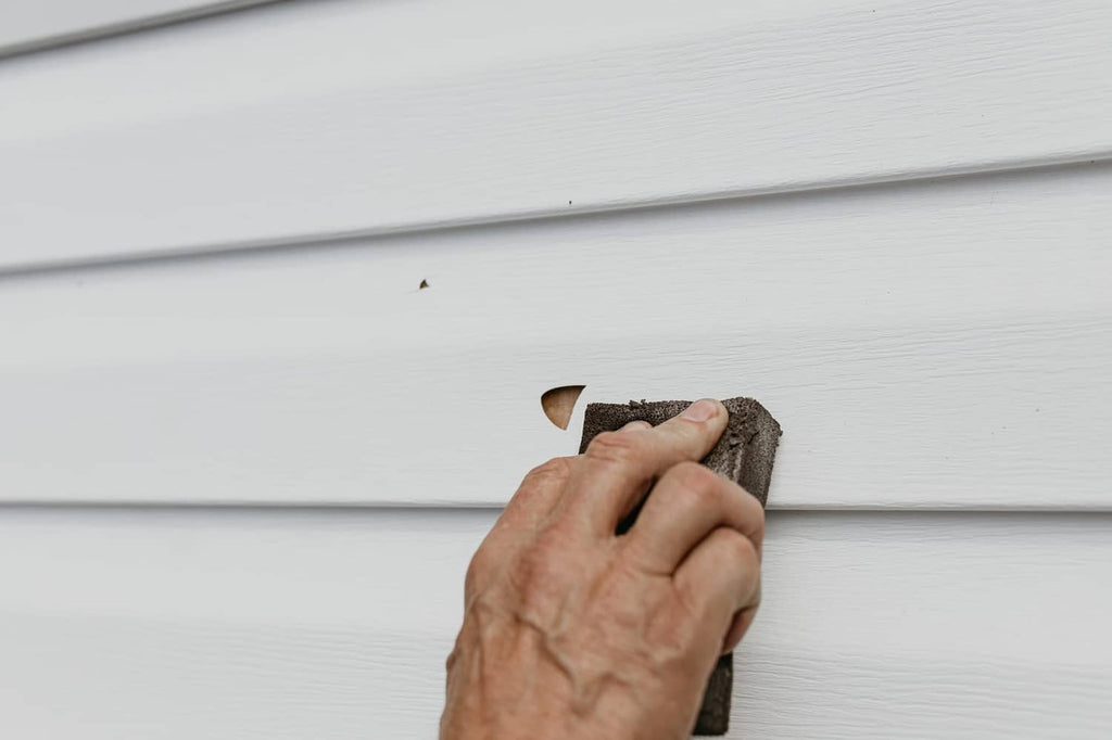 Mendyl vinyl siding repair: hand smoothing a patch area on white vinyl siding