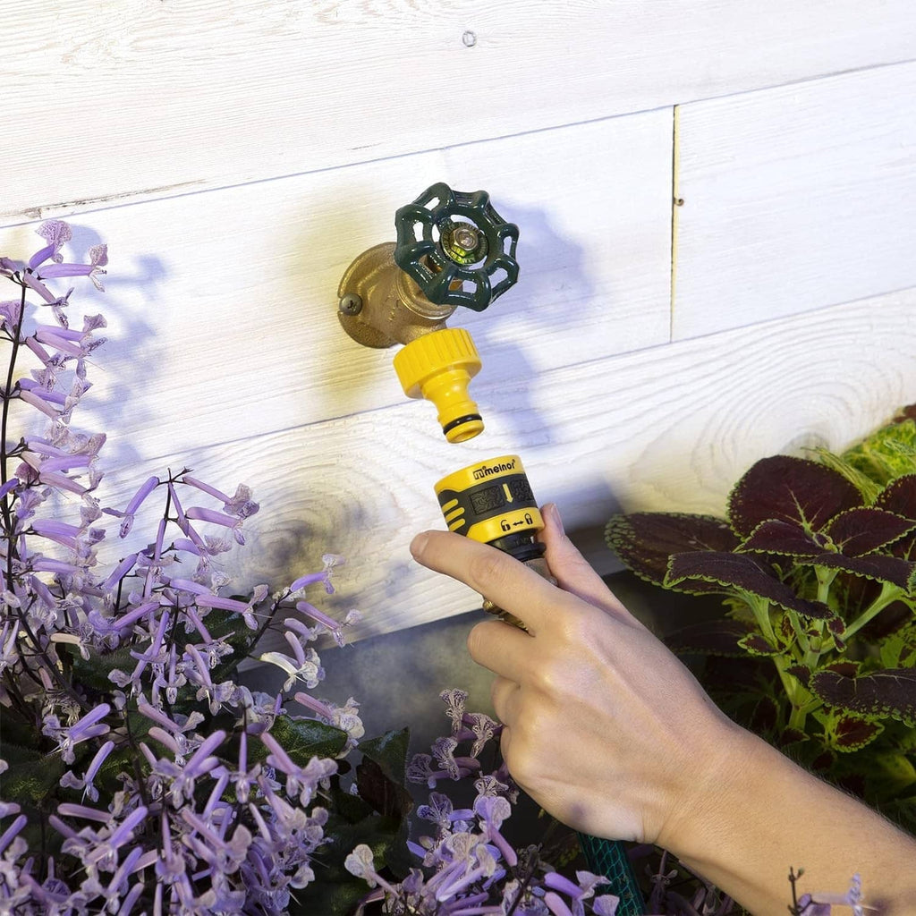 Quick Connect watering connector set with yellow nozzle and gray fittings near garden plants