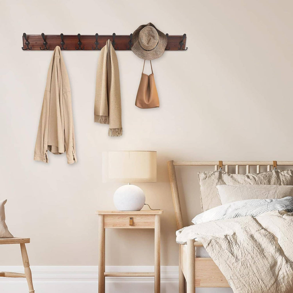 Wall-mounted coat rack with 10 black hooks on dark wood board holding coats and hat