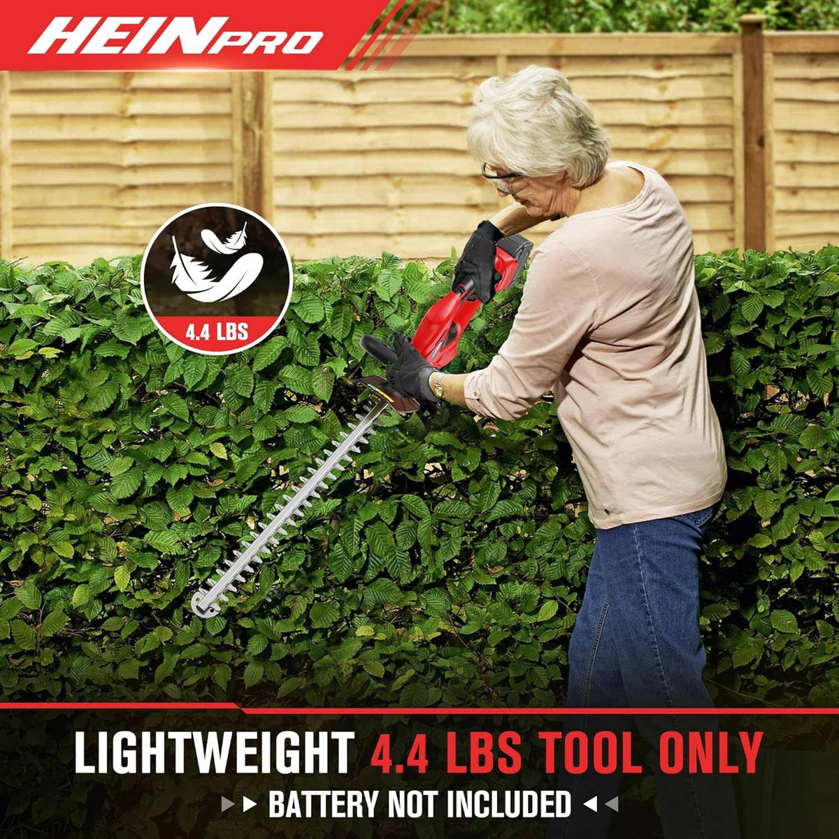Red cordless hedge trimmer cutting along the top of a green hedge