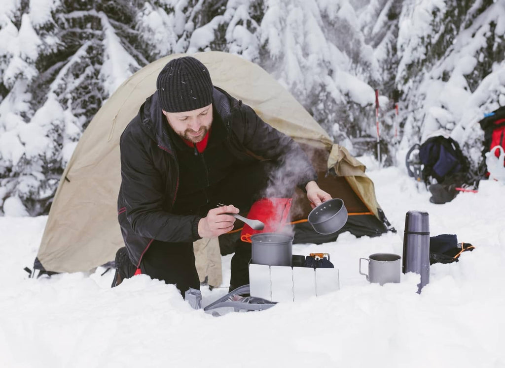 Camping stove in snow with aluminum windscreen panels around the cooking area
