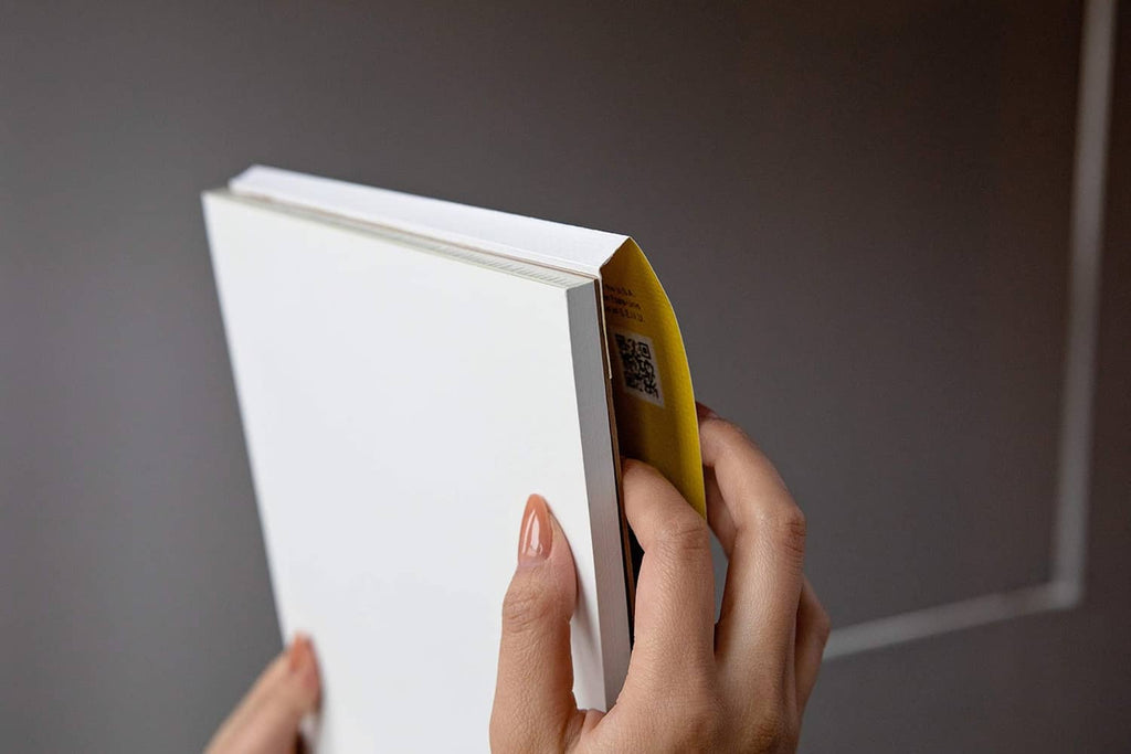 Tape-bound Bristol paper pad with yellow side edge, opened and held by hands.