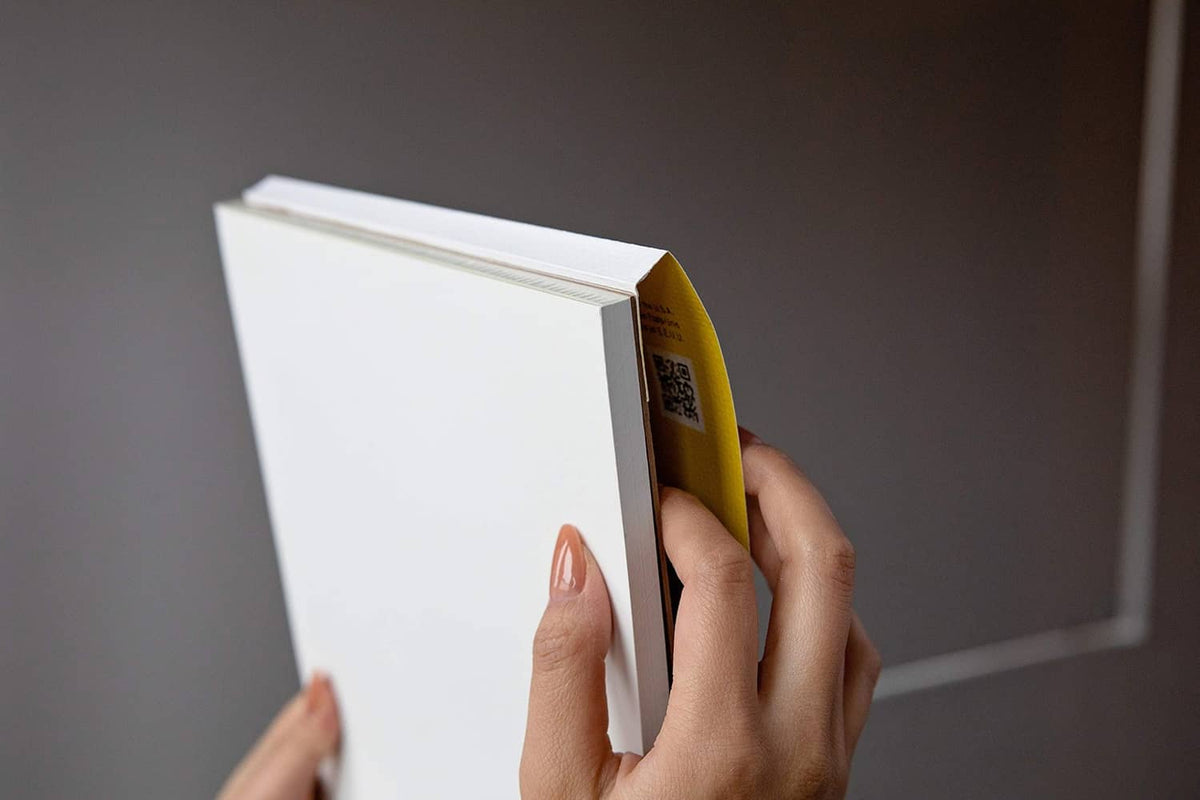 Tape-bound Bristol paper pad with yellow side edge, opened and held by hands.