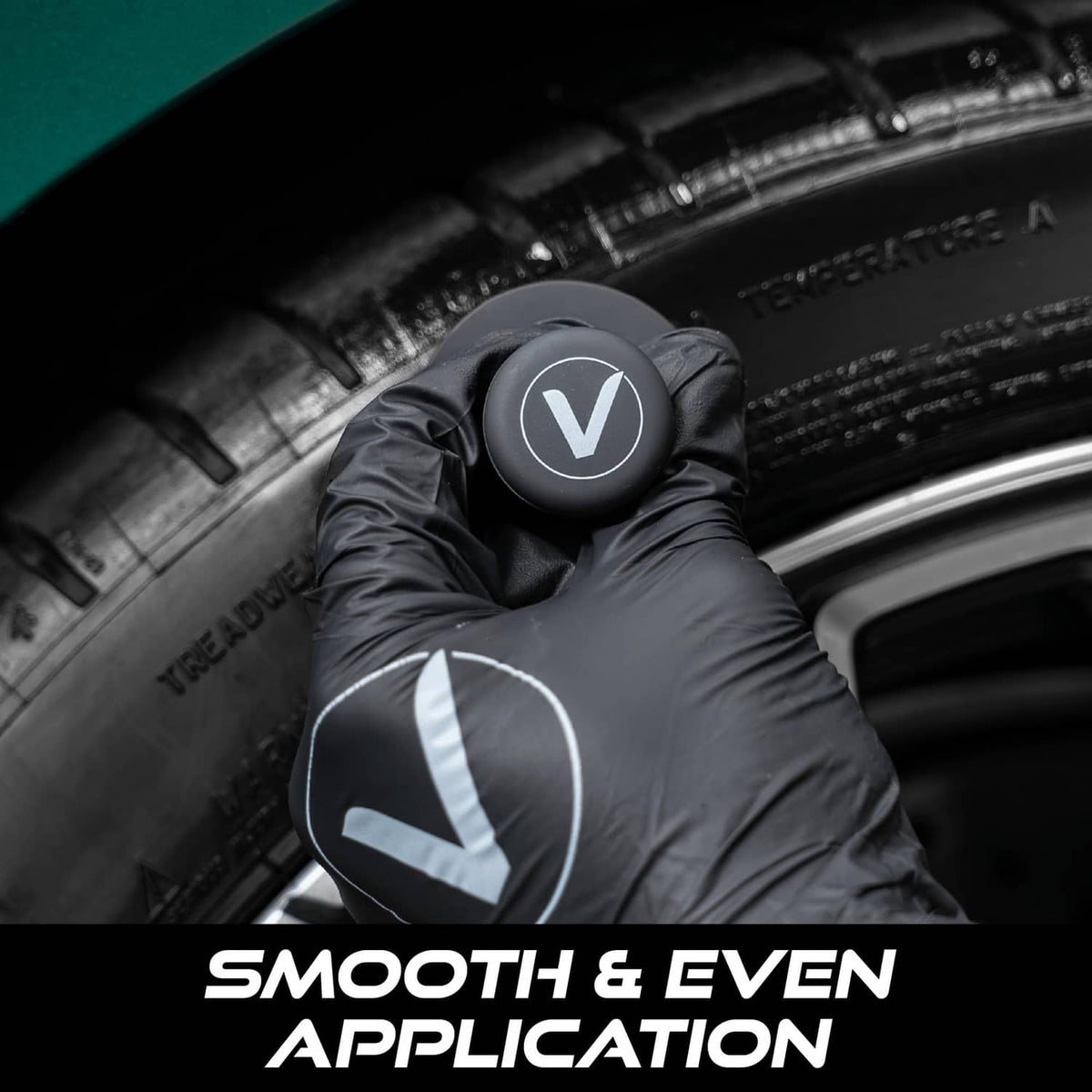 Black tire shine applicator brush held in gloved hands for smooth tire dressing