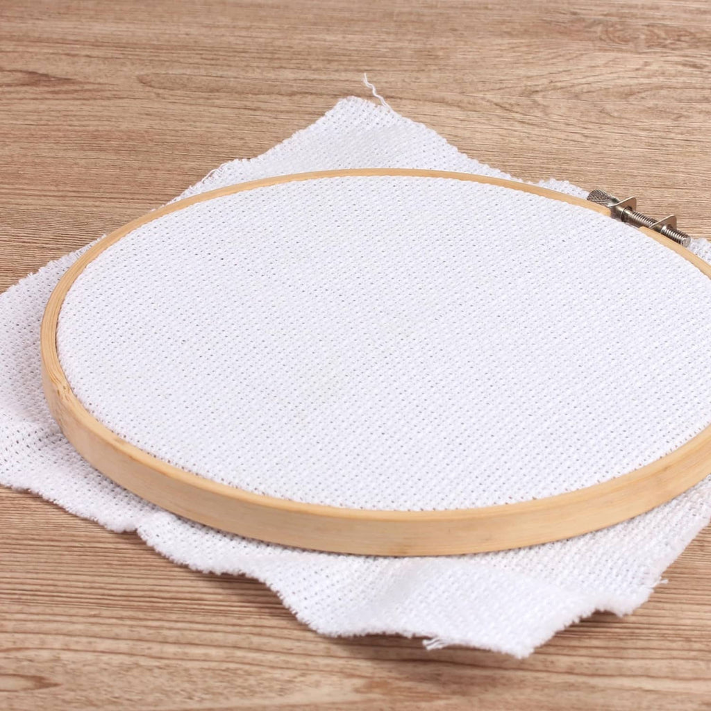 Bamboo embroidery hoop holding white fabric on a wooden surface