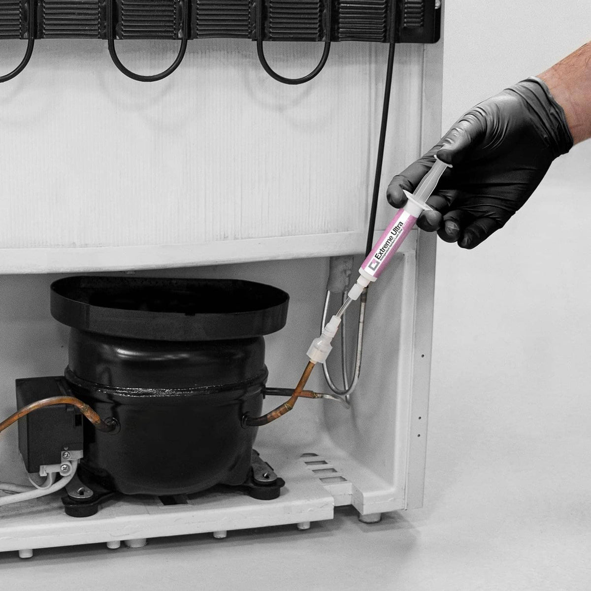 Technician applying sealant using a white injector syringe to a refrigeration compressor