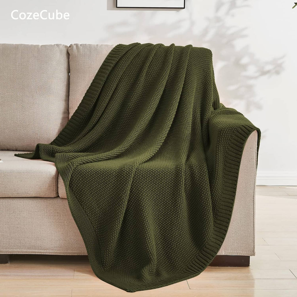 Olive green textured knit throw blanket draped over a sofa with soft folds.