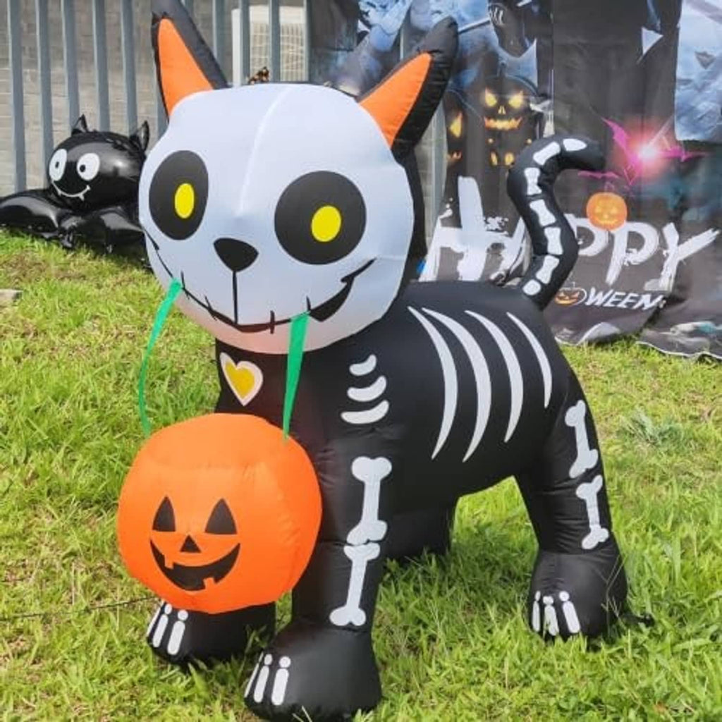 Close-up inflatable black cat with glowing pumpkin lantern and yellow eyes on grass