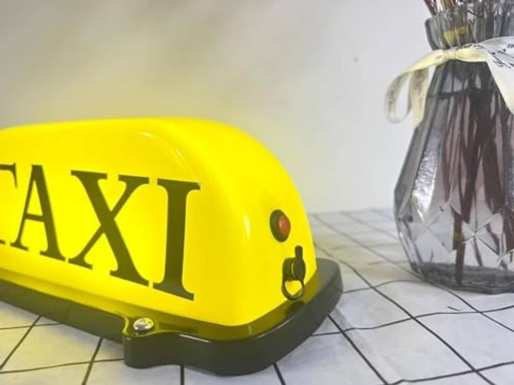 Close-up of yellow TAXI dome LED car sign light with side details and dark base