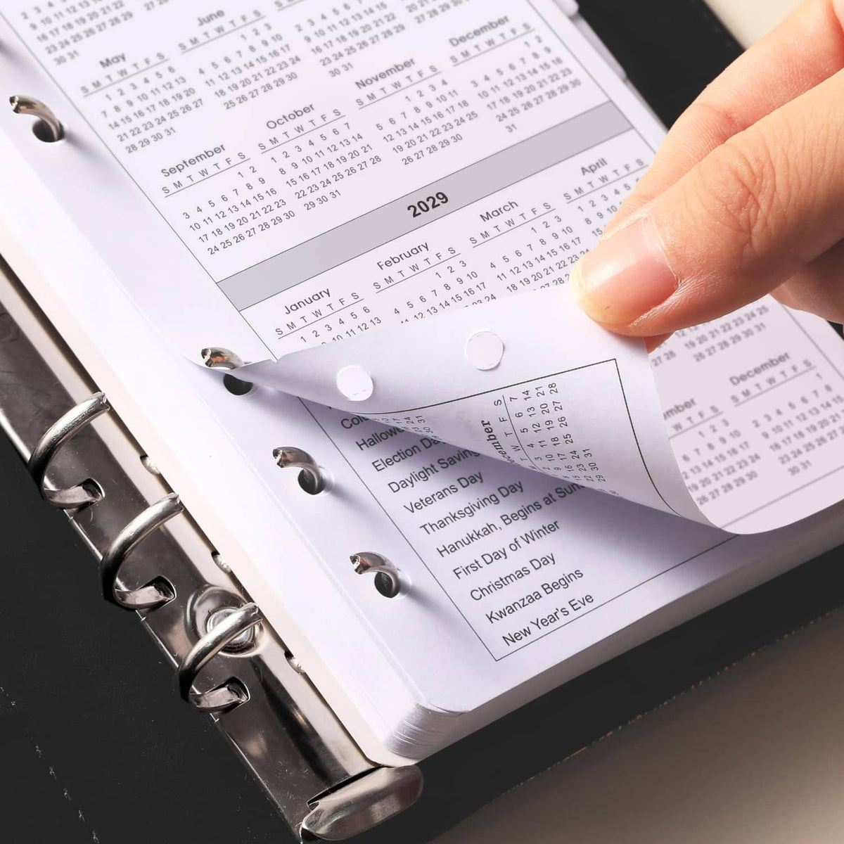 Hand holding an A6 monthly planner refill showing holiday list and day-of-week calendar grid