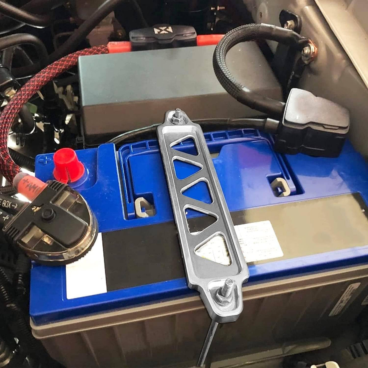 Silver battery hold-down bracket secured to a blue car battery with two J-hook anchors