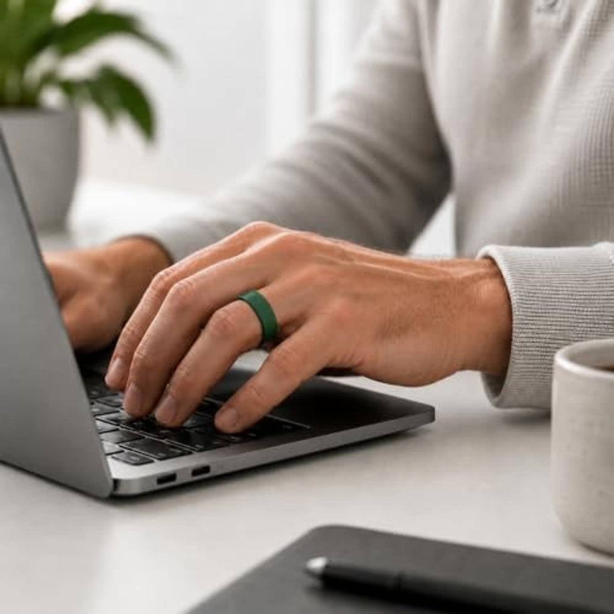 Green silicone ring cover for Oura Ring 5 on a hand while typing on a laptop