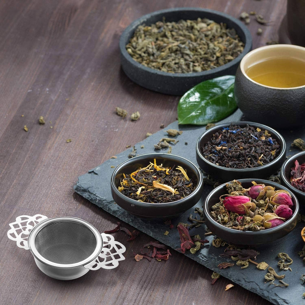 Mesh tea infuser with decorative handle beside small tea bowls