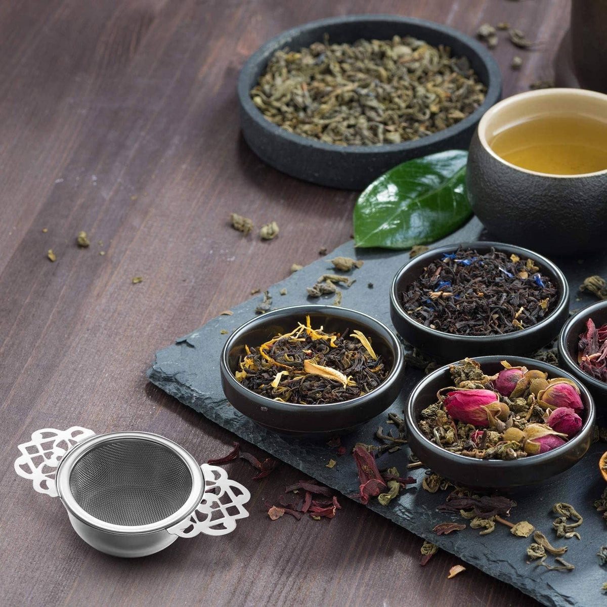 Mesh tea infuser with decorative handle beside small tea bowls