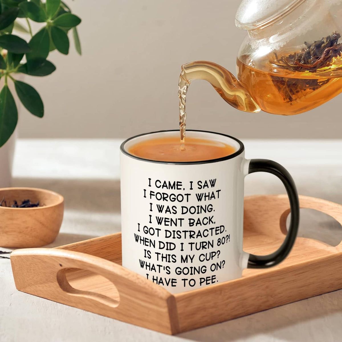 White mug with black handle and rim, 'turn 80' quote; tea pouring above.