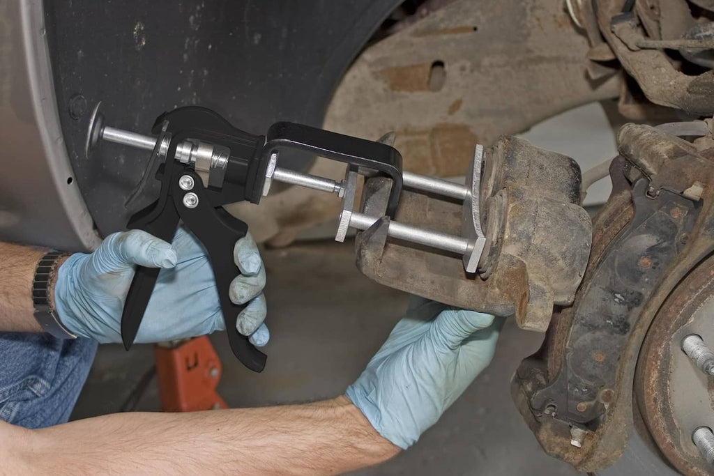 Brake pad spreader in use, gloved hands applying pressure near brake caliper