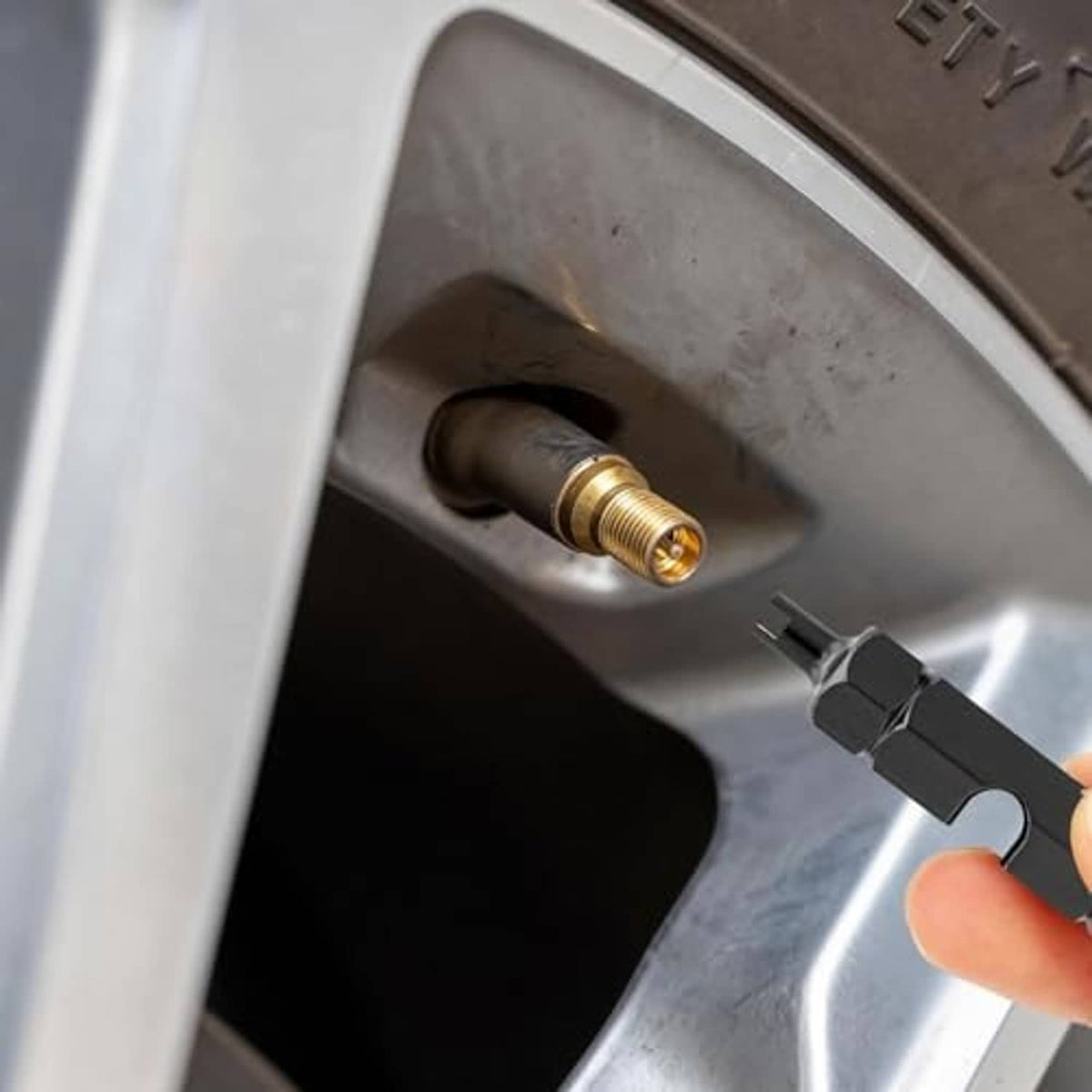 Black Presta valve core removal tool engaging a Presta valve stem on a wheel