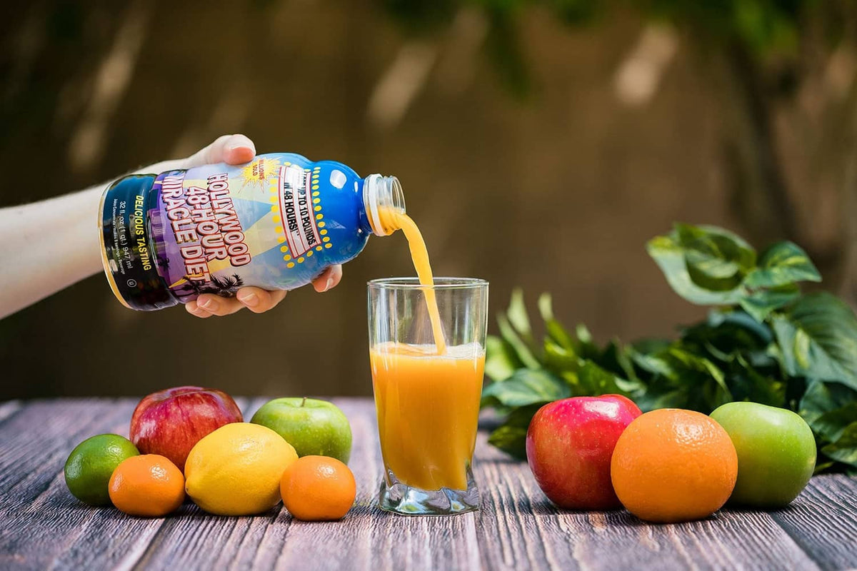 Bottle pouring orange juice into a glass with assorted fruits and vegetables