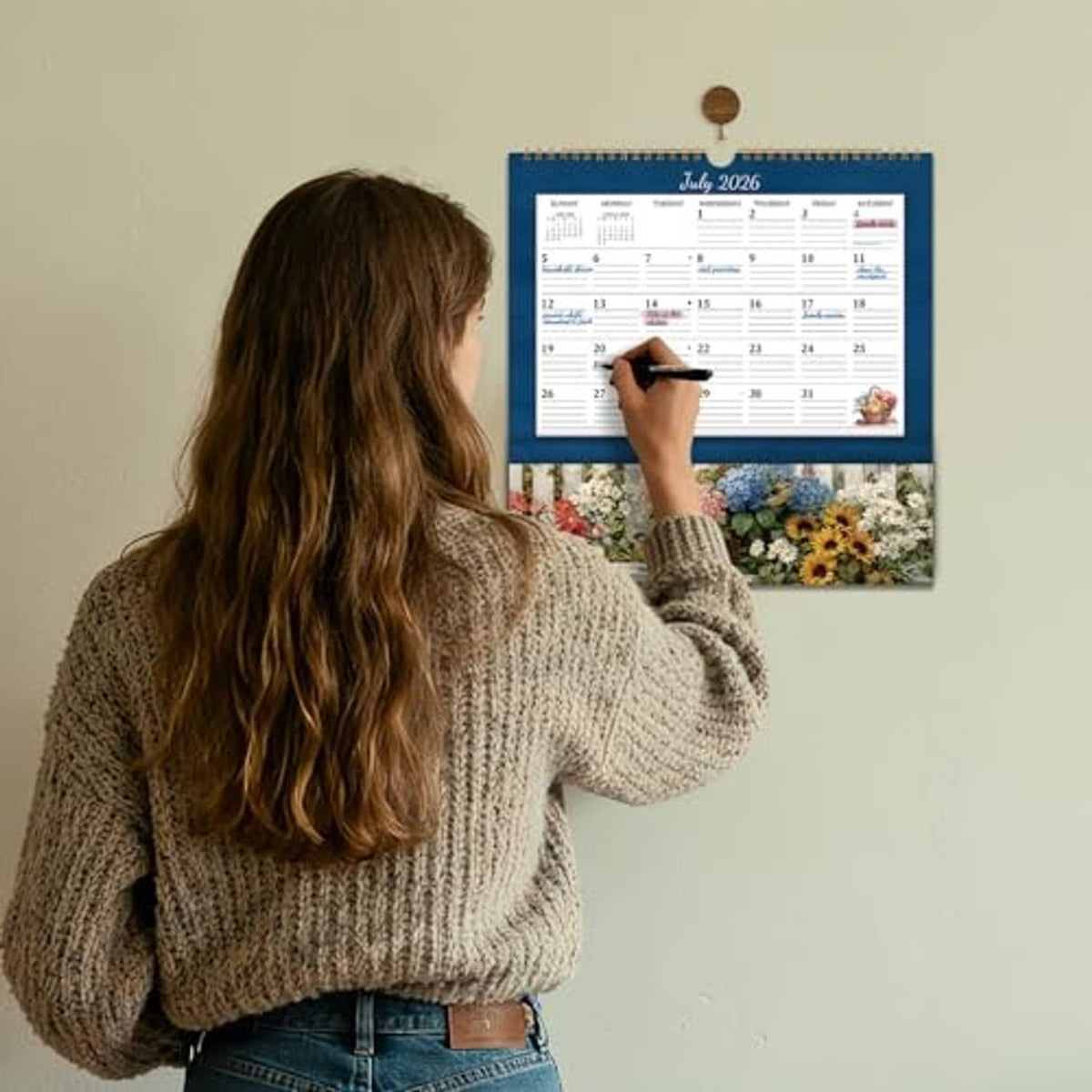 Wall calendar with pocket as a person marks dates on the July 2026 page
